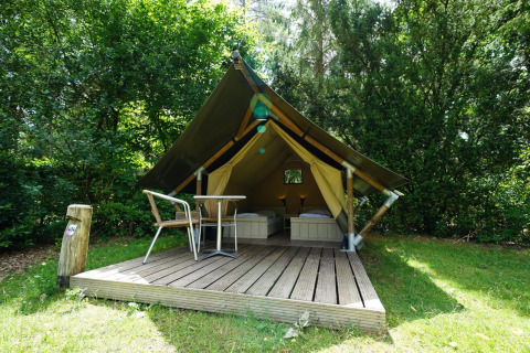 Mini-Glamping-Zelt mit Holzterrasse, zwei Betten und Sitzbereich inmitten eines grünen Waldgebietes.