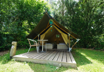 Mini glamping telt med terrasse og to senge, placeret i grønne omgivelser for en komfortabel naturoplevelse.