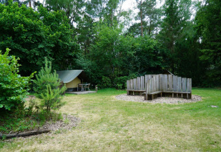 Mini glampingtent bij De Wije Werelt in Nederland, houten zitbank en veel bomen rondom de open plek.