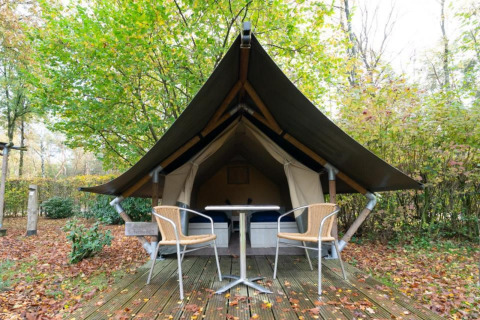 Mini tienda glamping safari en De Wije Werelt, Países Bajos, con terraza, sillas y bosque frondoso.