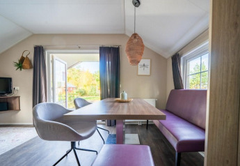 Moderne spiseplads i Boslodge på De Wije Werelt i Holland med lilla bænk, stole og store vinduer.