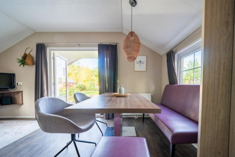 Moderne spiseplads i Boslodge på De Wije Werelt i Holland med lilla bænk, stole og store vinduer.
