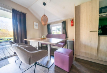 Moderne eetruimte in Boslodge bij De Wije Werelt, Nederland, met paarse zitplaatsen en uitzicht buiten.