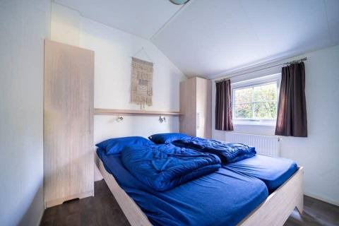 Soveværelse på Boslodge på De Wije Werelt i Holland med blå sengetøj, indbyggede skabe og vindue.