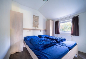 Schlafzimmer in der Boslodge bei De Wije Werelt in den Niederlanden, mit blauer Bettwäsche und Fensterausblick.