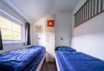 Zimmer in der Boslodge bei De Wije Werelt in den Niederlanden mit zwei Einzelbetten und blauer Bettwäsche.