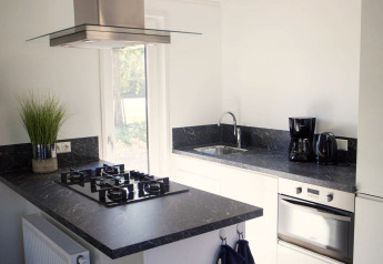 Moderne keuken met zwarte werkbladen, gasvuur, oven en koffiezetapparaat in Velthorst, De Wije Werelt.