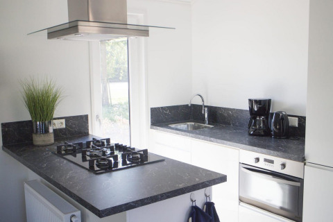 Cocina moderna con encimera negra, estufa de gas, horno y cafetera en Velthorst, De Wije Werelt.