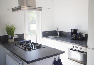 Cocina moderna con encimera negra, estufa de gas, horno y cafetera en Velthorst, De Wije Werelt.