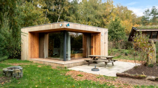Lodge moderne en bois nommé Fred, en pleine nature, avec grandes baies vitrées, terrasse et feu de camp.