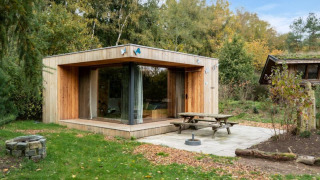 Lodge moderne en bois nommé Fred, en pleine nature, avec grandes baies vitrées, terrasse et feu de camp.
