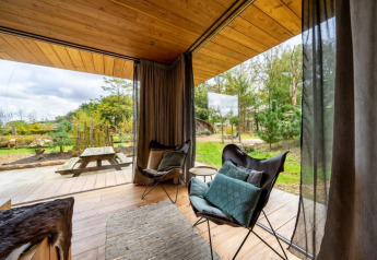 Udsigt fra lodge Fred på De Wije Werelt i Holland med komfortable stole og naturudsigt gennem glasvæg.