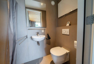 Baño moderno en la cabaña Fred de De Wije Werelt, Países Bajos, con inodoro suspendido y lavabo pequeño.