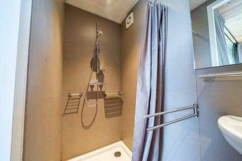 Douche moderne avec rideau dans le lodge Fred à De Wije Werelt, Pays-Bas, avec barres d’appui murales.