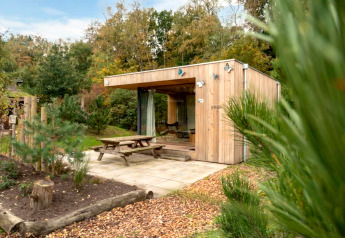 Wooden lodge named Fred at De Wije Werelt in the Netherlands, set among trees with a picnic table outside.