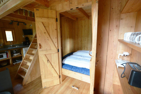 Interior de pequeña casa de madera con cama y cocina en Treehouse at De Wije Werelt, Países Bajos.