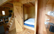 Træhytteinteriør med kompakt soveplads og køkken, fotograferet i Treehouse at De Wije Werelt, Holland.