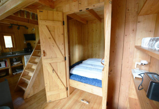 Interior de pequeña casa de madera con cama y cocina en Treehouse at De Wije Werelt, Países Bajos.