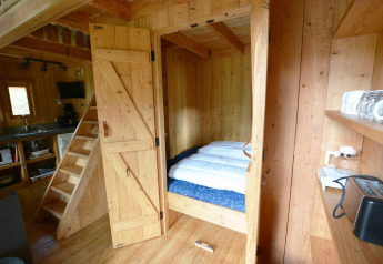 Gezellige tiny house met houten interieur, bed in nis en keuken in Treehouse at De Wije Werelt, Nederland.