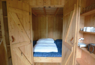 Acogedor rincón para dormir con cama doble tras puertas de madera en una tiny house en Treehouse De Wije Werelt.