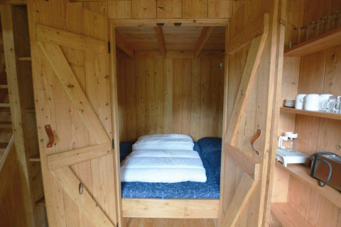 Angolo notte accogliente con letto matrimoniale dietro porte in legno nella tiny house Treehouse De Wije Werelt.