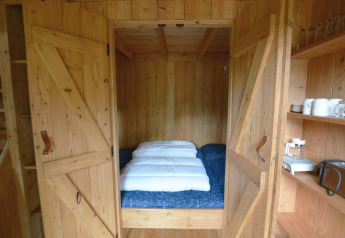 Angolo notte accogliente con letto matrimoniale dietro porte in legno nella tiny house Treehouse De Wije Werelt.