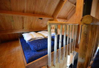 Cama en altillo con ropa de cama azul en la casa del árbol de De Wije Werelt, Países Bajos.