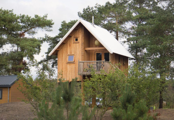 Una pequeña casa de árbol con balcón y techo blanco, rodeada de pinos en De Wije Werelt, Países Bajos.