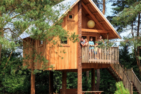 Famiglia sulla balconata di una casa sull’albero a De Wije Werelt, immersa nel verde nei Paesi Bassi.