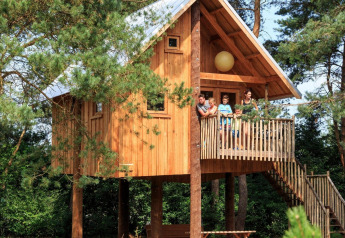 Family standing on the balcony of a wooden treehouse at De Wije Werelt, surrounded by forest in the Netherlands.