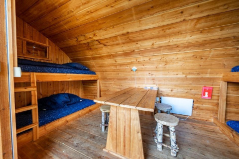 Interior de la tiny house Geurt en De Wije Werelt, Países Bajos, con literas, mesa y taburetes rústicos.