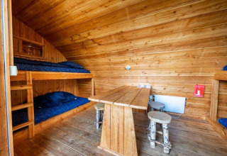 Interior de la tiny house Geurt en De Wije Werelt, Países Bajos, con literas, mesa y taburetes rústicos.