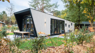 Lodge moderne à Just Nature avec grandes baies vitrées, coin repas extérieur et verdure tout autour.