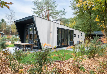 Lodge moderne à Just Nature avec grandes baies vitrées, coin repas extérieur et verdure tout autour.