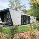 Moderne lodge bij Just Nature met grote ramen, buitenzitje en omgeven door groene natuur en bomen.