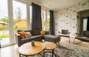Moderne woonkamer in Just Nature-lodge op De Wije Werelt, Nederland, met grote ramen en stijlvolle inrichting.