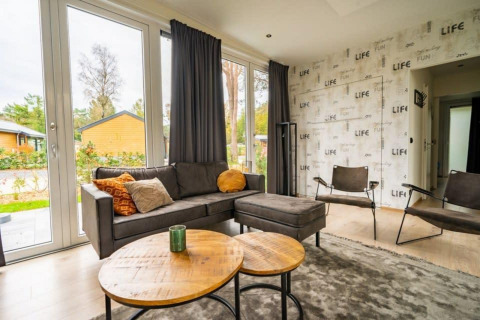 Moderne woonkamer in Just Nature-lodge op De Wije Werelt, Nederland, met grote ramen en stijlvolle inrichting.