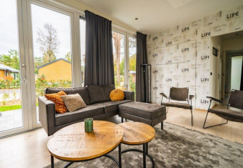 Modernes Wohnzimmer der Just Nature Lodge in De Wije Werelt, Niederlande, mit großen Fenstern und Blick auf die Natur.