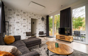 Stue i lodge ved Just Nature, De Wije Werelt, Holland med store vinduer, sofa, tv og hyggeligt interiør.