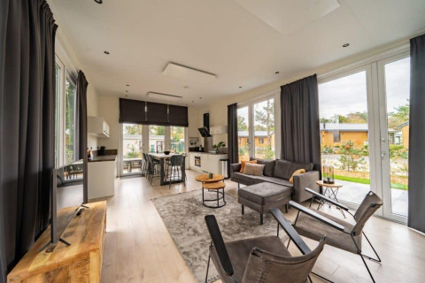 Moderne Lodge Just Nature in De Wije Werelt, Niederlande, mit hellem Wohnbereich und großen Fenstern.