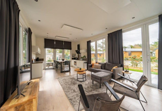 Moderne lodge Just Nature bij De Wije Werelt, Nederland, met lichte zithoek en grote ramen.