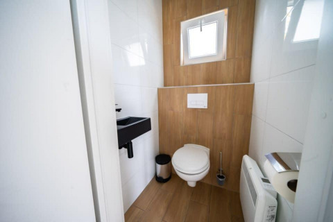 Baño moderno con suelo de madera, pequeño lavabo y ventana en Just Nature, De Wije Werelt, Países Bajos.