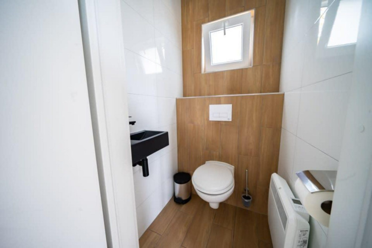 Baño moderno con suelo de madera, pequeño lavabo y ventana en Just Nature, De Wije Werelt, Países Bajos.