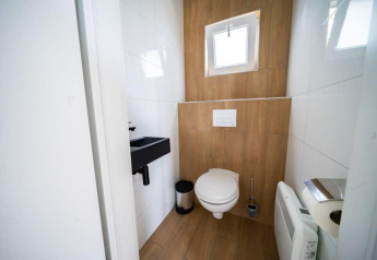 Baño moderno con suelo de madera, pequeño lavabo y ventana en Just Nature, De Wije Werelt, Países Bajos.