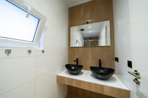 Baño moderno con dos lavabos negros, espejo grande y ventana en Just Nature, De Wije Werelt, Países Bajos.