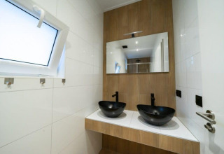 Baño moderno con dos lavabos negros, espejo grande y ventana en Just Nature, De Wije Werelt, Países Bajos.