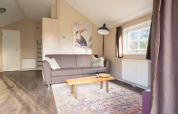 Stue i Boslodge ved De Wije Werelt i Holland med sofa, kunstværk af tukan, bord og stort vindue.