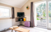 Lyst interiør i Boslodge på De Wije Werelt i Holland med tv, sofabord og udsigt til have og picnicbord.