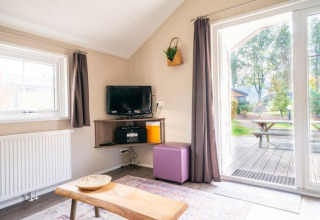 Lyst interiør i Boslodge på De Wije Werelt i Holland med tv, sofabord og udsigt til have og picnicbord.