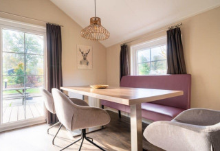 Dining area in the Boslodge at De Wije Werelt, Netherlands. Bright room with table, chairs, bench, and large windows.